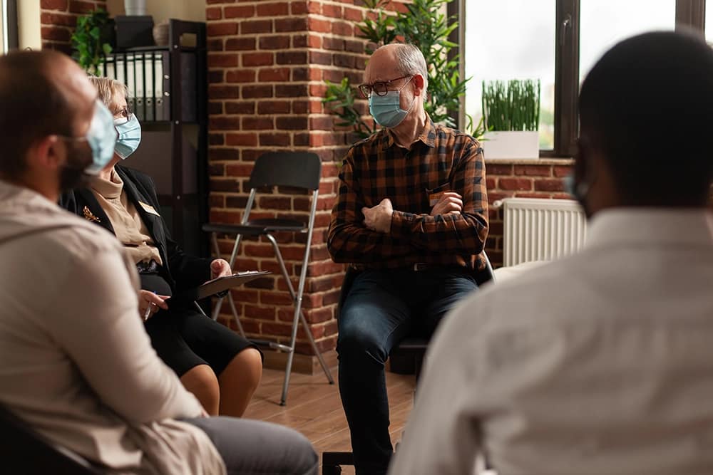 Group gathering with older man wearing a mask.